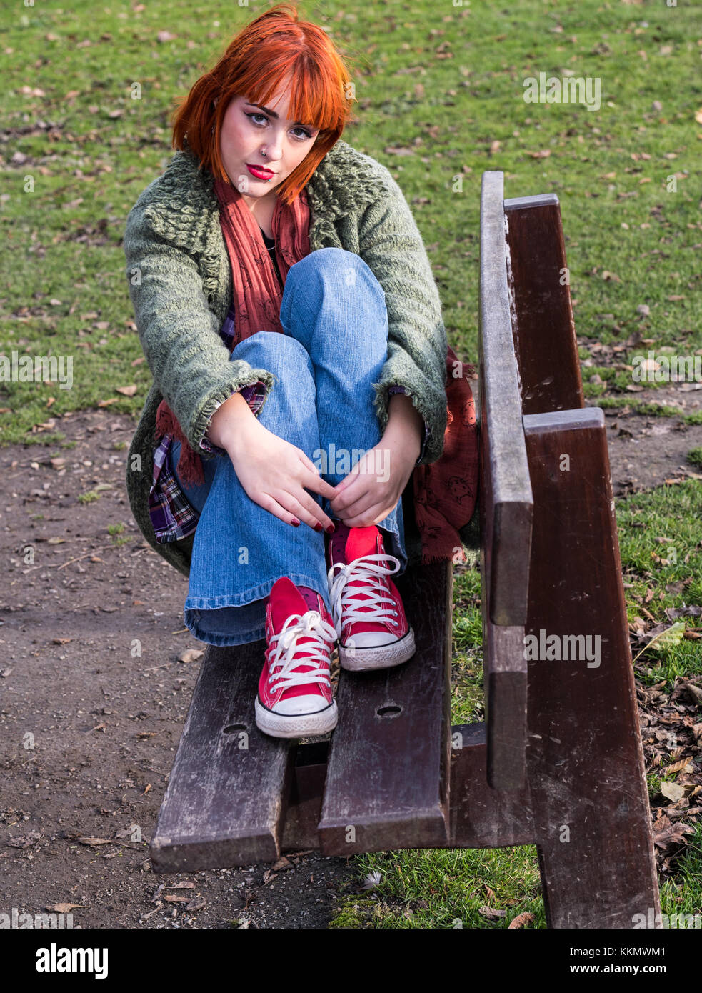 Chica pelirroja en un banco en el parque en otoño Foto de stock