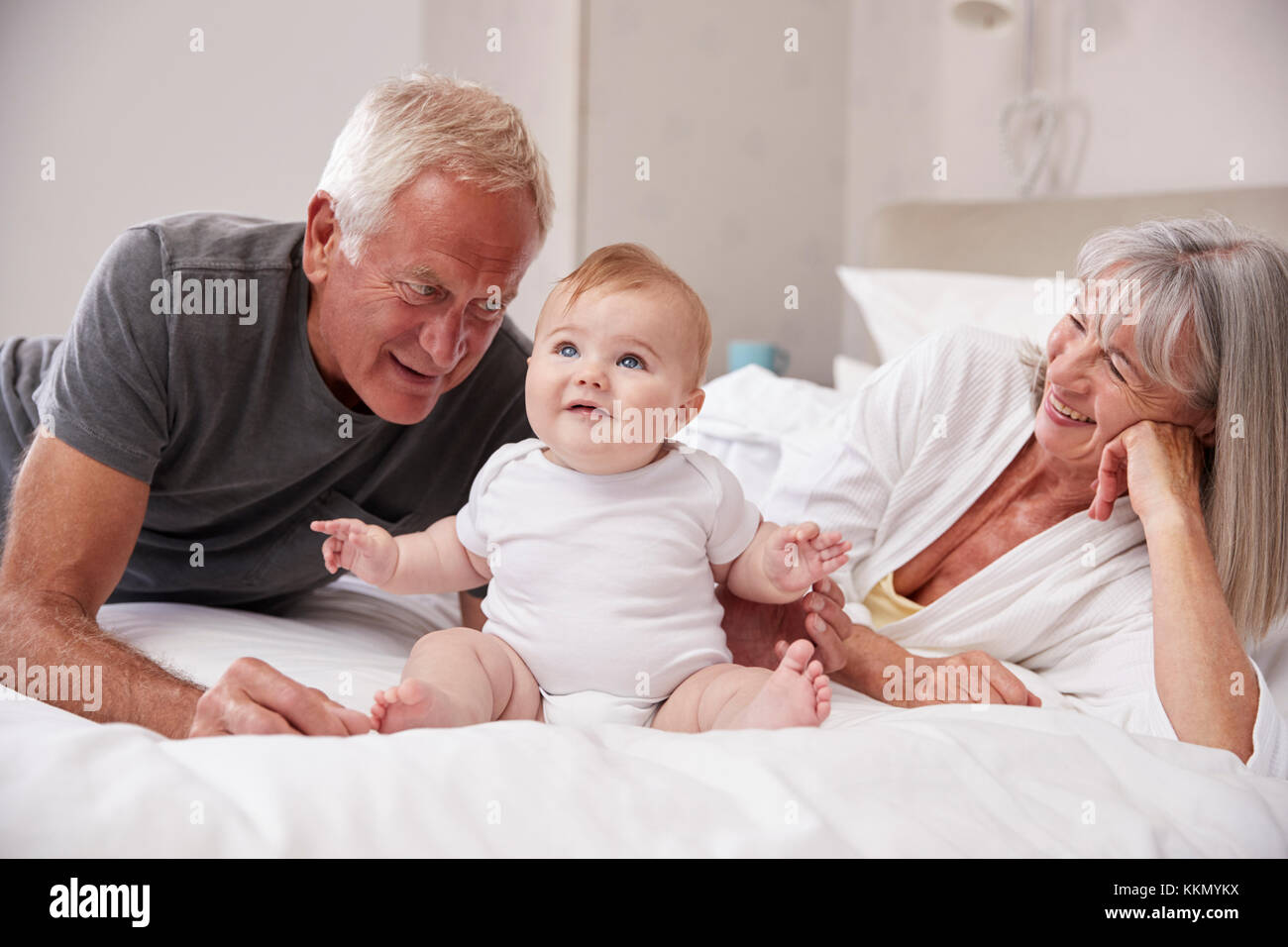 Los abuelos tumbado en la cama en casa cuidando de bebé nieto Foto de stock