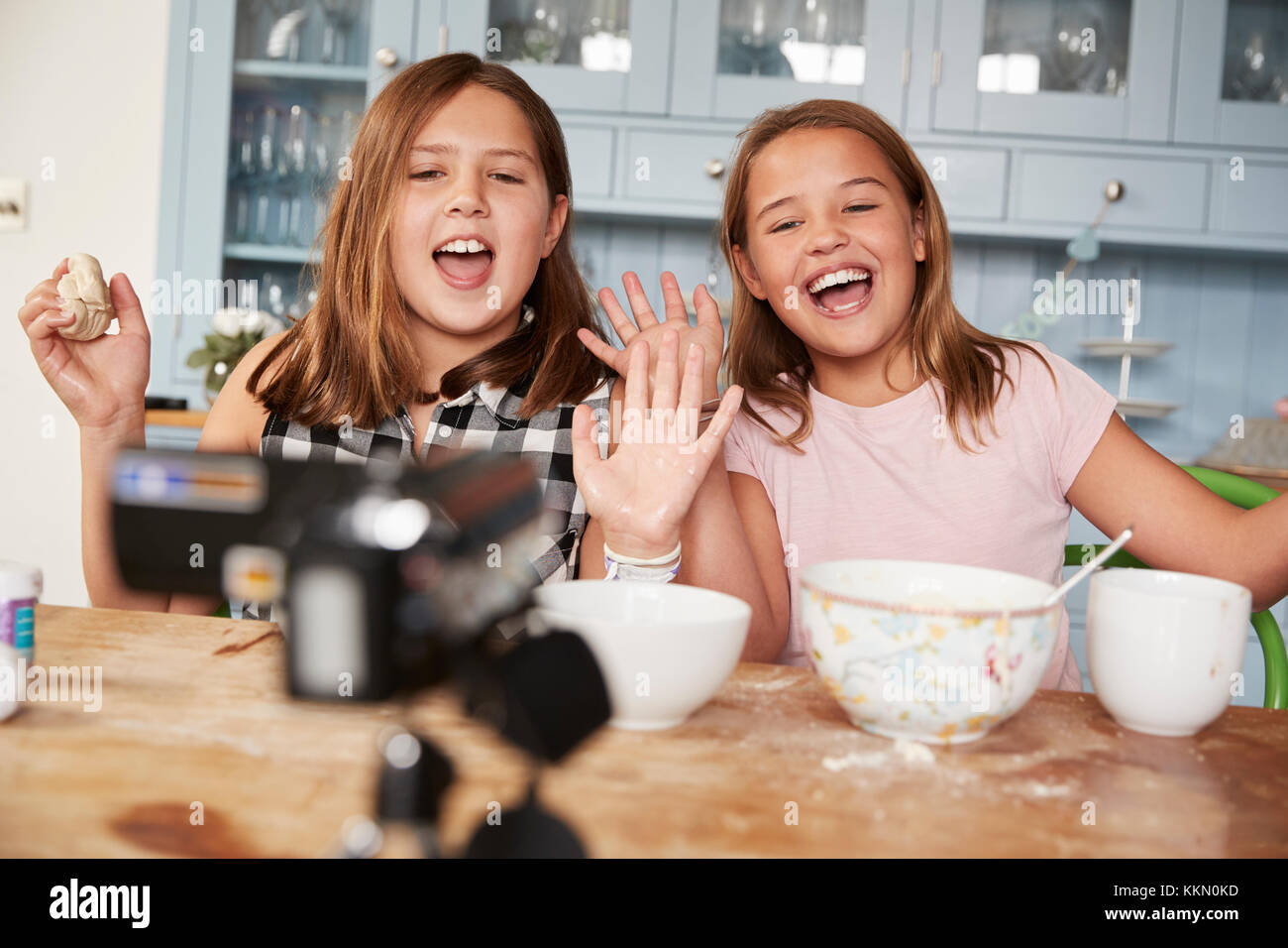 Dos pre-adolescentes video blogging en la cocina saludando a la cámara Foto de stock