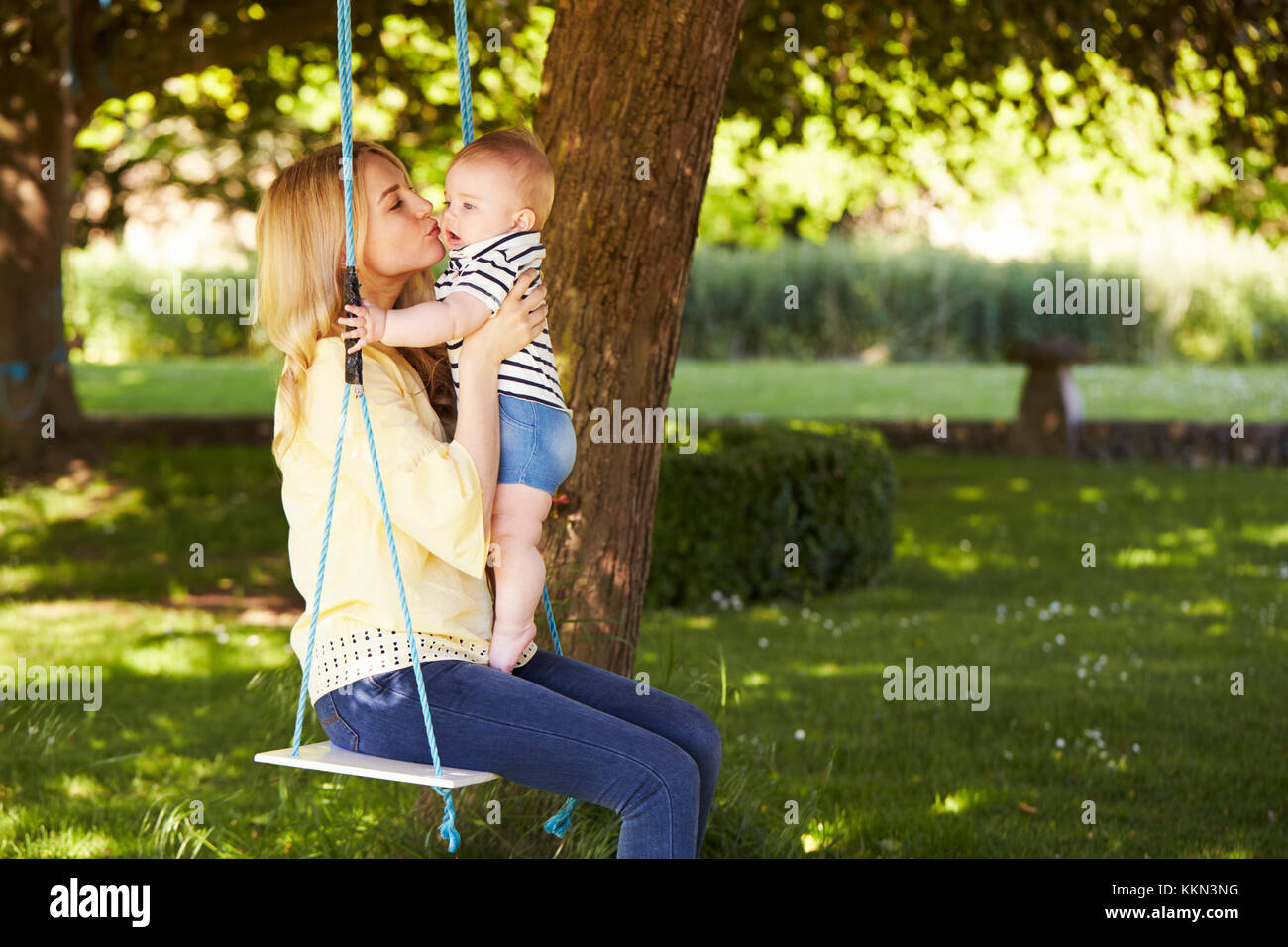 Madre besando a su hijo mientras se sientan en el balancín de jardín Foto de stock