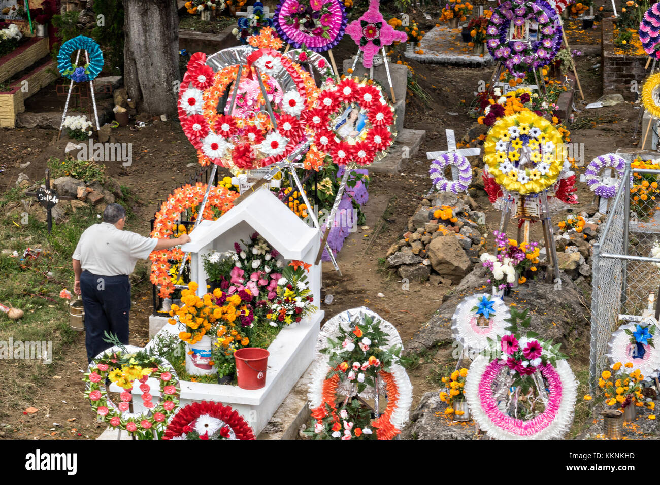 Un hombre se detiene en una tumba decorada con guirnaldas y flores para