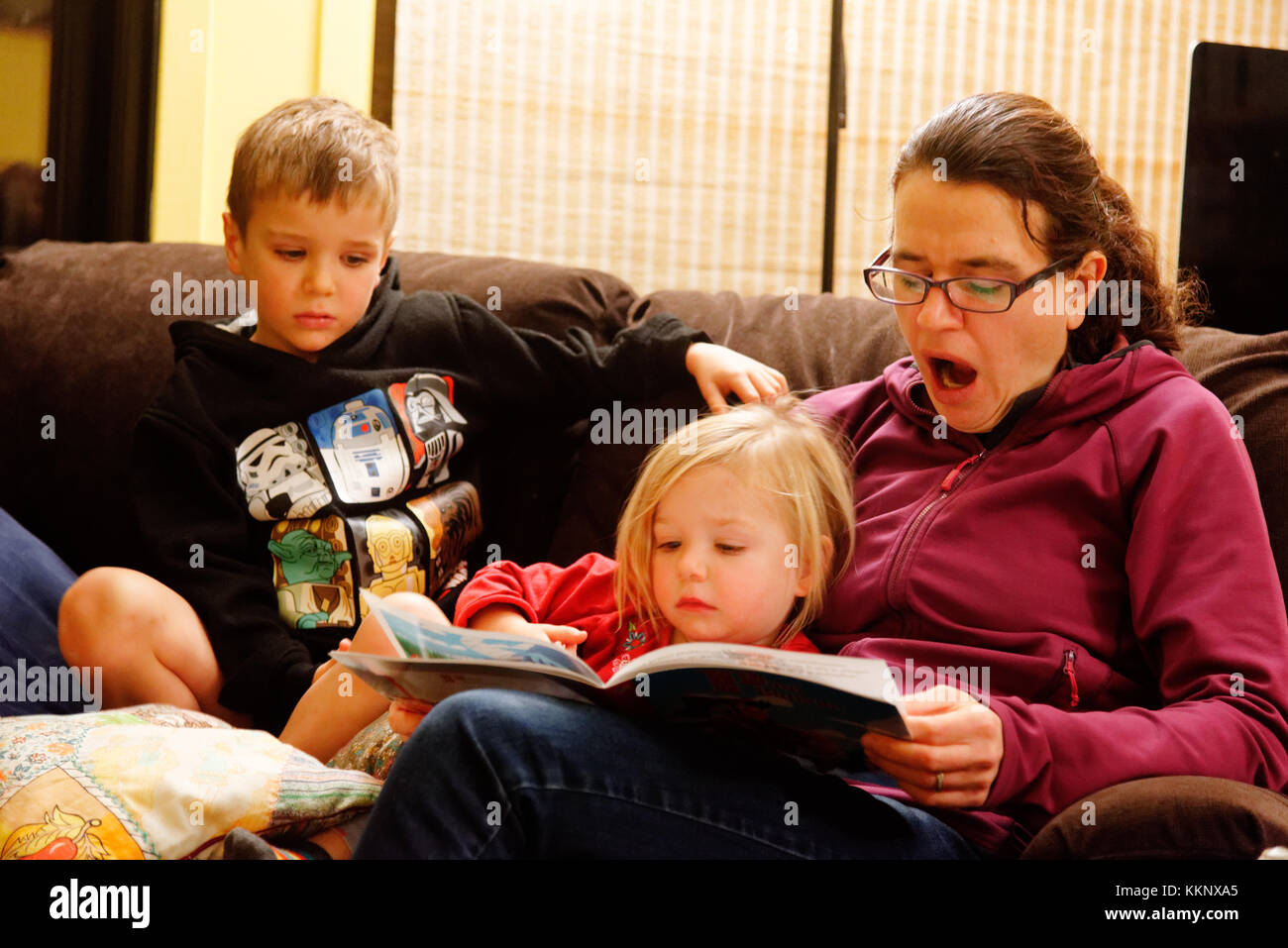 Una madre cansada bostezo mientras leía en voz alta a sus hijos (de 5 y 3 años) Foto de stock