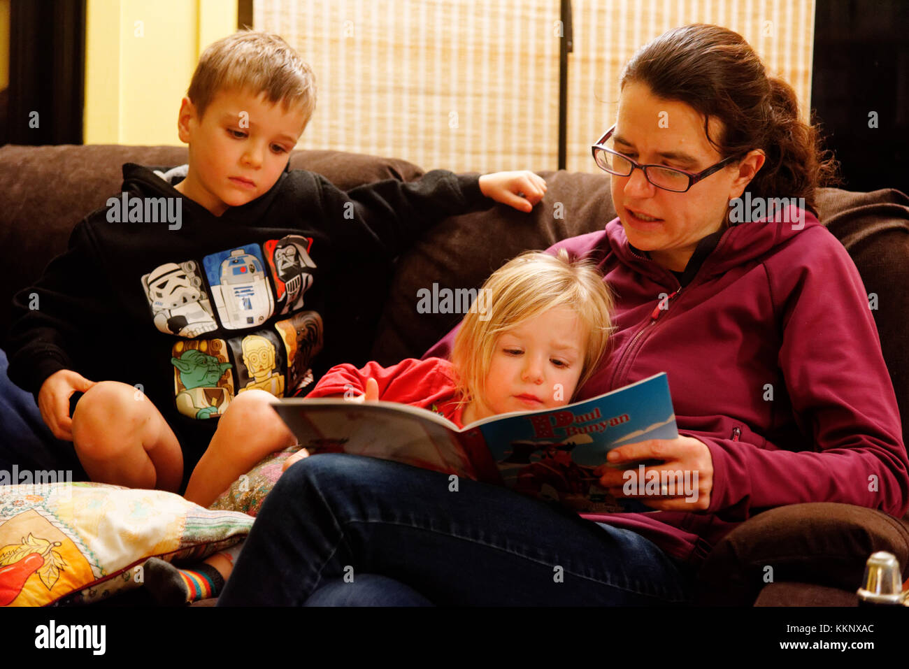 Una madre leyendo en voz alta a sus dos hijos (de 5 y 3 años) Foto de stock