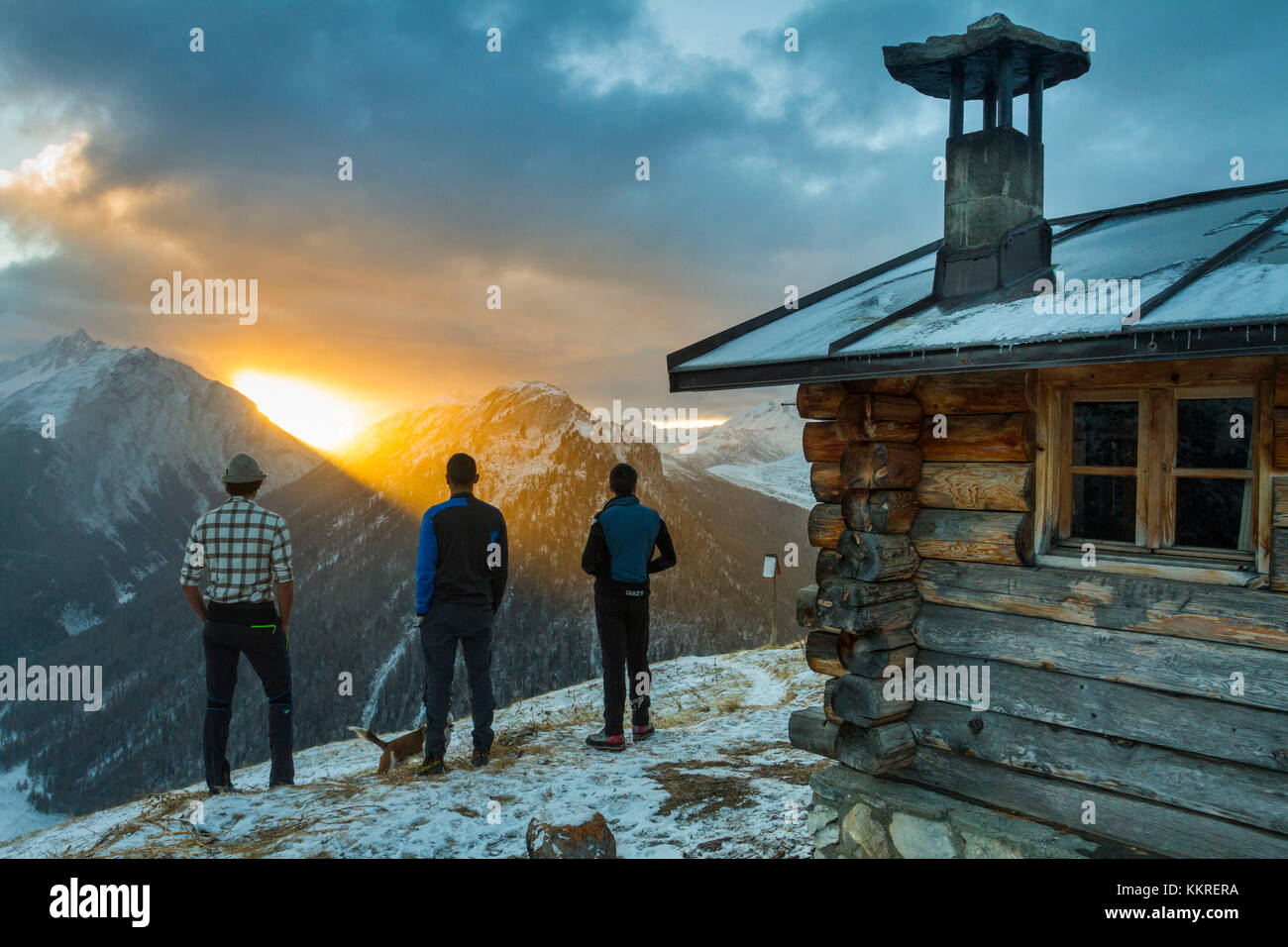 Tres amigos admirando el amanecer desde una cabaña alpina. Livigno, Valtellina, Italia Foto de stock