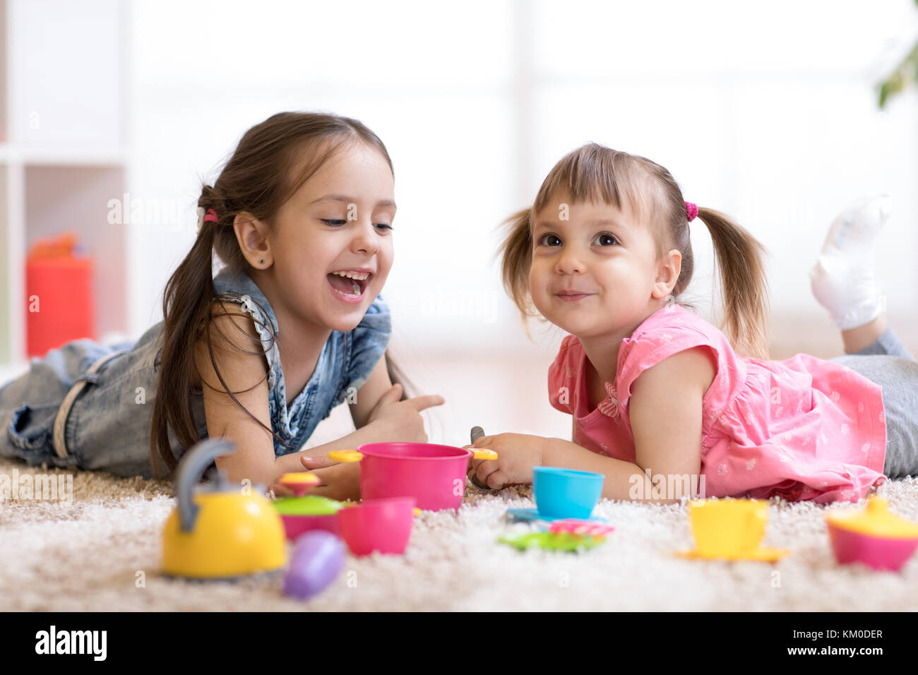 Cute little niños jugando con menaje mientras yacían en el suelo en casa Foto de stock