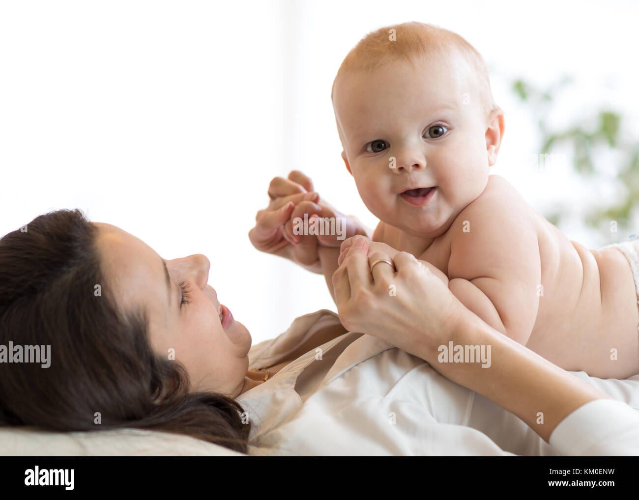 La madre y el bebé abrazándolo y jugar acostado en interiores Foto de stock