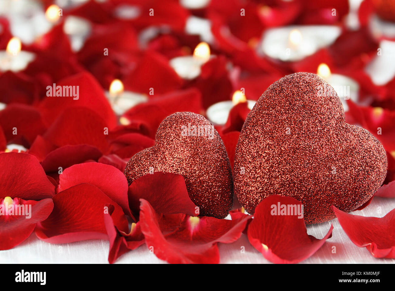 Día de San Valentín corazones rodeado de pétalos de rosa y velas lite contra un fondo blanco. Habitación para copiar el espacio con gran profundidad de campo. Foto de stock