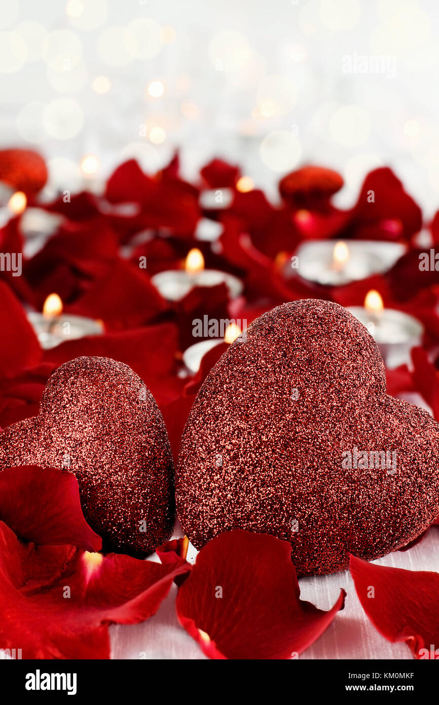 Día de San Valentín corazones rodeado de pétalos de rosa y velas lite contra un fondo blanco. Habitación para copiar el espacio con gran profundidad de campo. Foto de stock