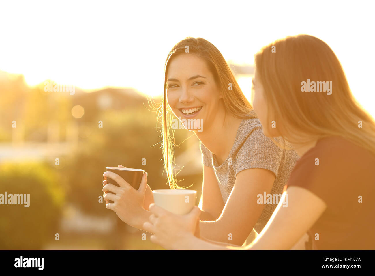 Dos amigos hablando fuera feliz en un balcón de la casa al atardecer Foto de stock