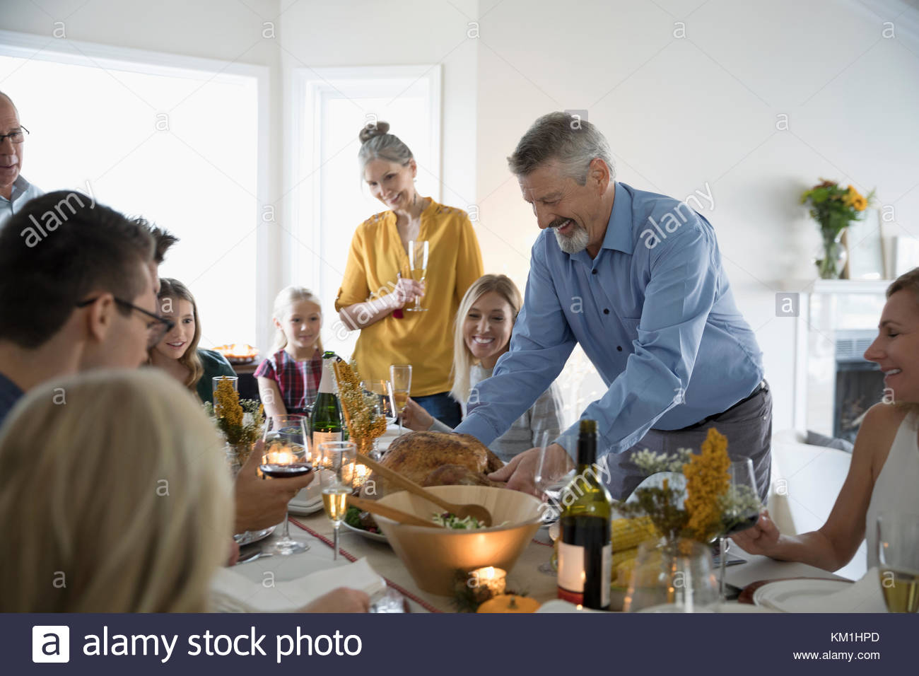Hombre sirviendo pavo de Acción de Gracias con su familia y amigos en mesa Foto de stock