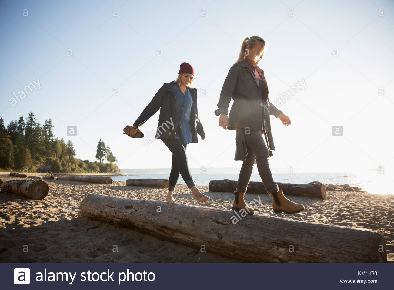 Madre e hija caminando, equilibrando en registro en la soleada playa. Foto de stock