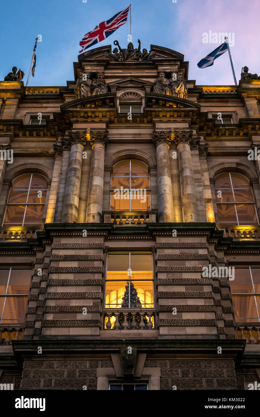Edificio victoriano Banco de Escocia, la sede, el montículo, iluminado al anochecer con el árbol de Navidad en la ventana y banderas, Edimburgo, Escocia, Reino Unido Foto de stock