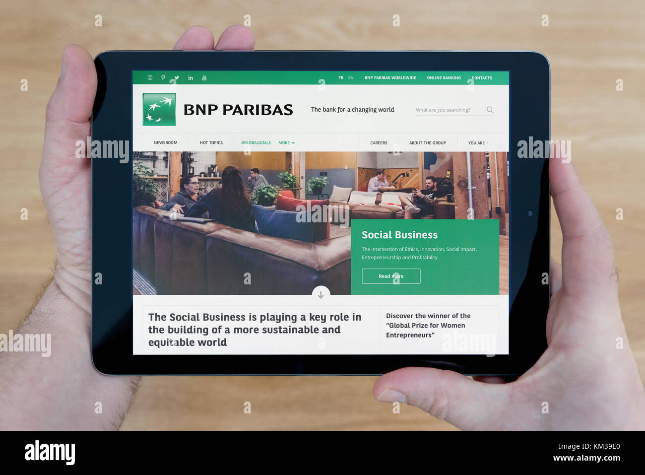Un hombre se ve en el sitio web del banco BNP Paribas en su iPad dispositivo tablet, disparó contra una mesa de madera fondo superior (uso Editorial solamente) Foto de stock