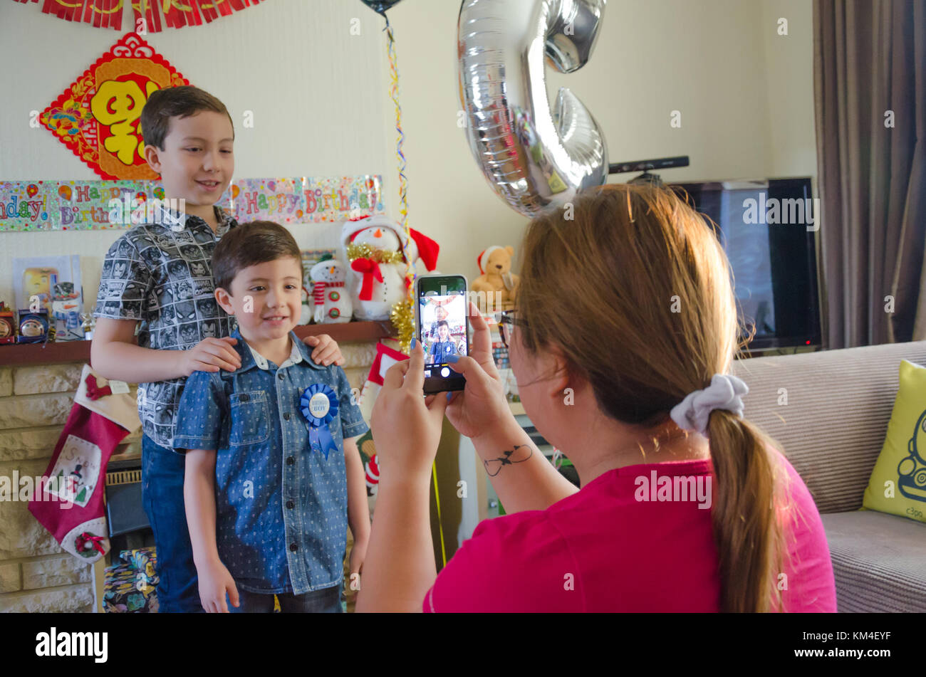 Una madre toma una foto en su iphone de sus dos hijos con ocasión del cumpleaños del hijo menor, Foto de stock