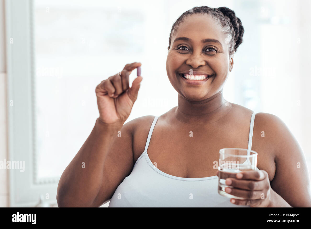 Mujer africana sonriente sosteniendo una píldora y vaso de agua Foto de stock