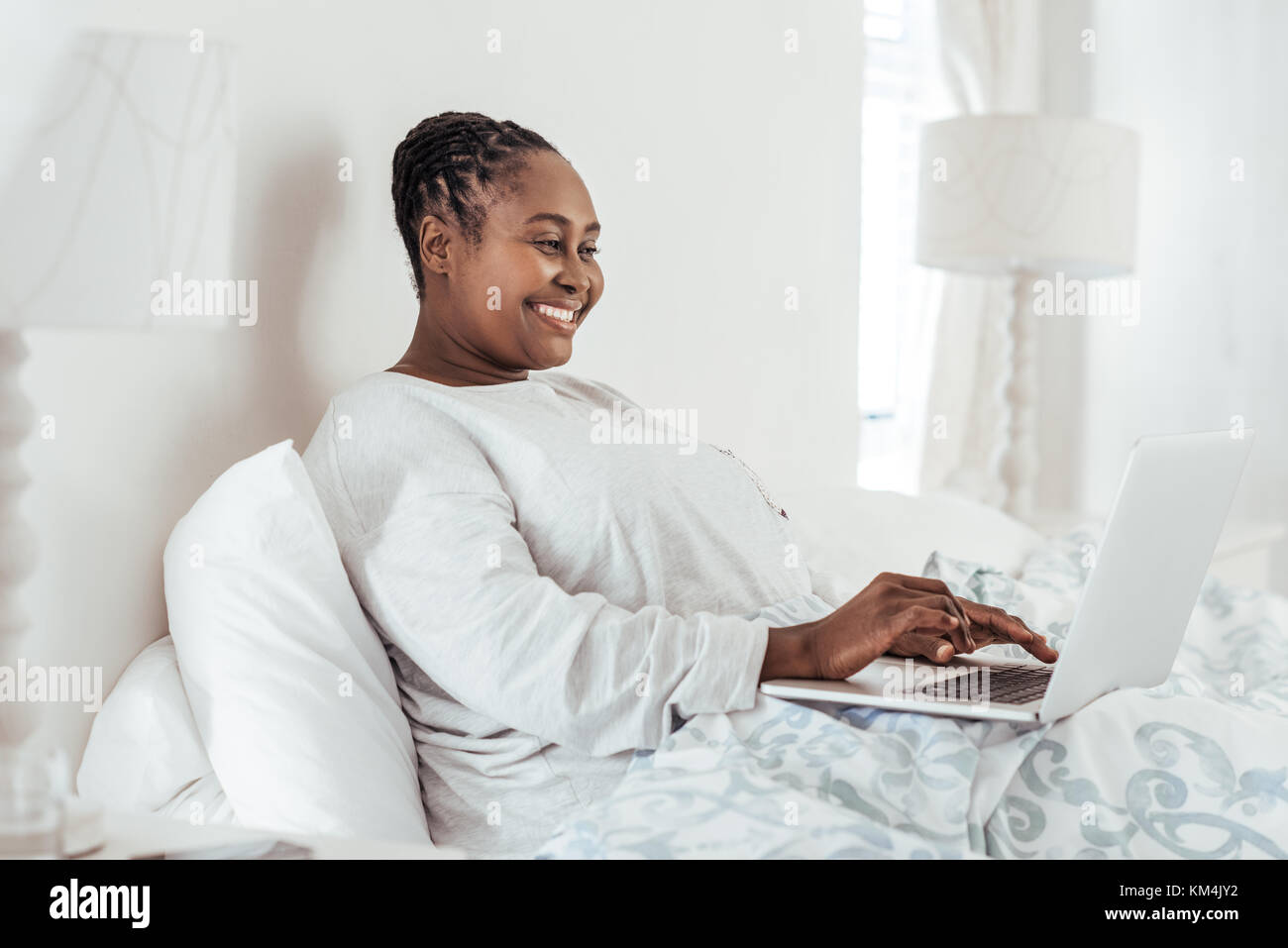 Sonriente mujer africana acostado en la cama con un portátil Foto de stock