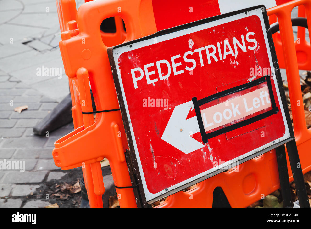 Las barreras de la calle rojas en un borde del lugar de construcción con peatones mire flecha izquierda Foto de stock