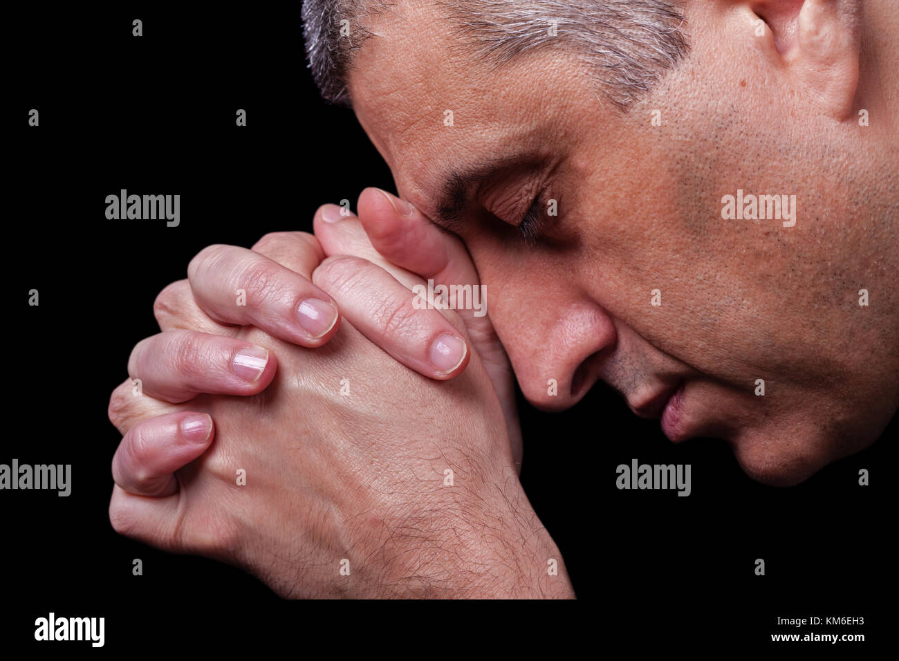 Cerca de fieles hombre maduro orando manos plegadas adorar a Dios con la cabeza hacia abajo y los ojos cerrados en fondo negro religiosa la religión cristiana vertical Foto de stock