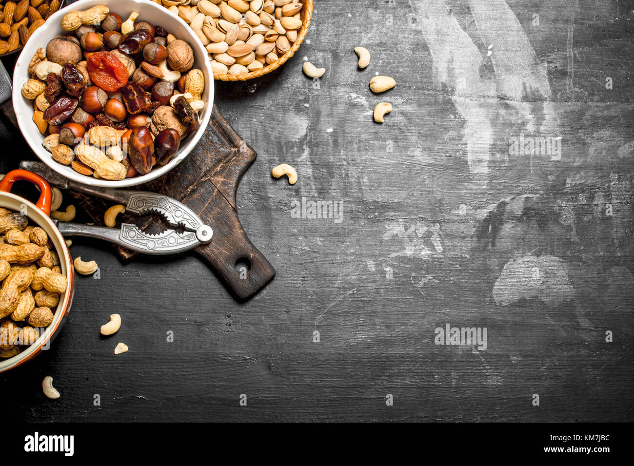 Nueces y frutos secos en un recipiente con un cascanueces. sobre una pizarra negra. Foto de stock
