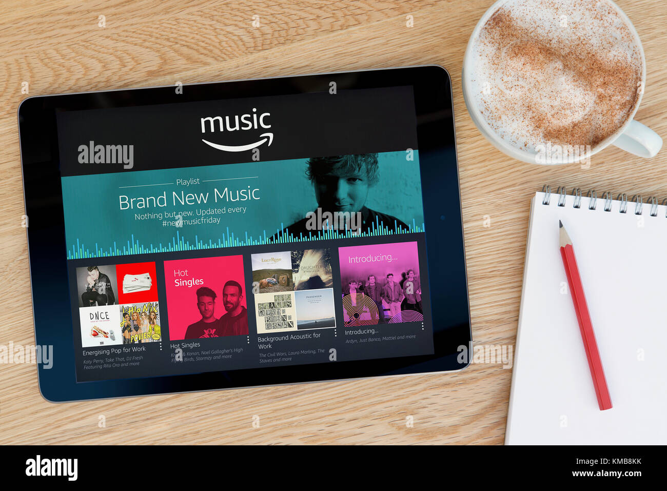 Amazon Music app características en un dispositivo tablet iPad que descansa sobre una mesa de madera junto a un bloc de notas y lápiz y una taza de café (Editorial). Foto de stock