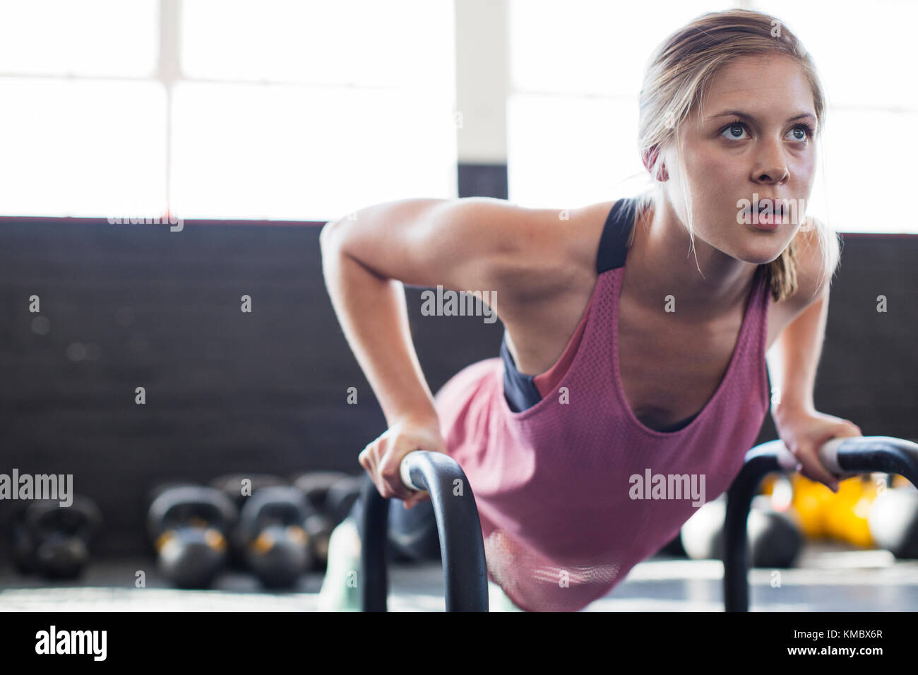 Retrato determinada, mujer joven enfocada haciendo flexiones con equipo en el gimnasio Foto de stock
