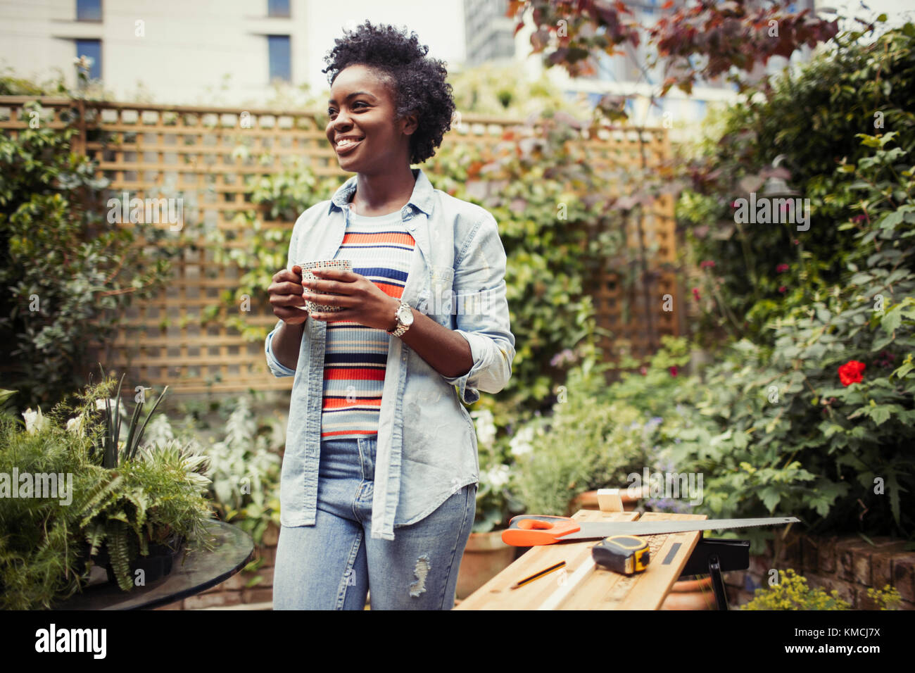 Mujer sonriente bebiendo café y haciendo un proyecto de bricolaje en el patio Foto de stock