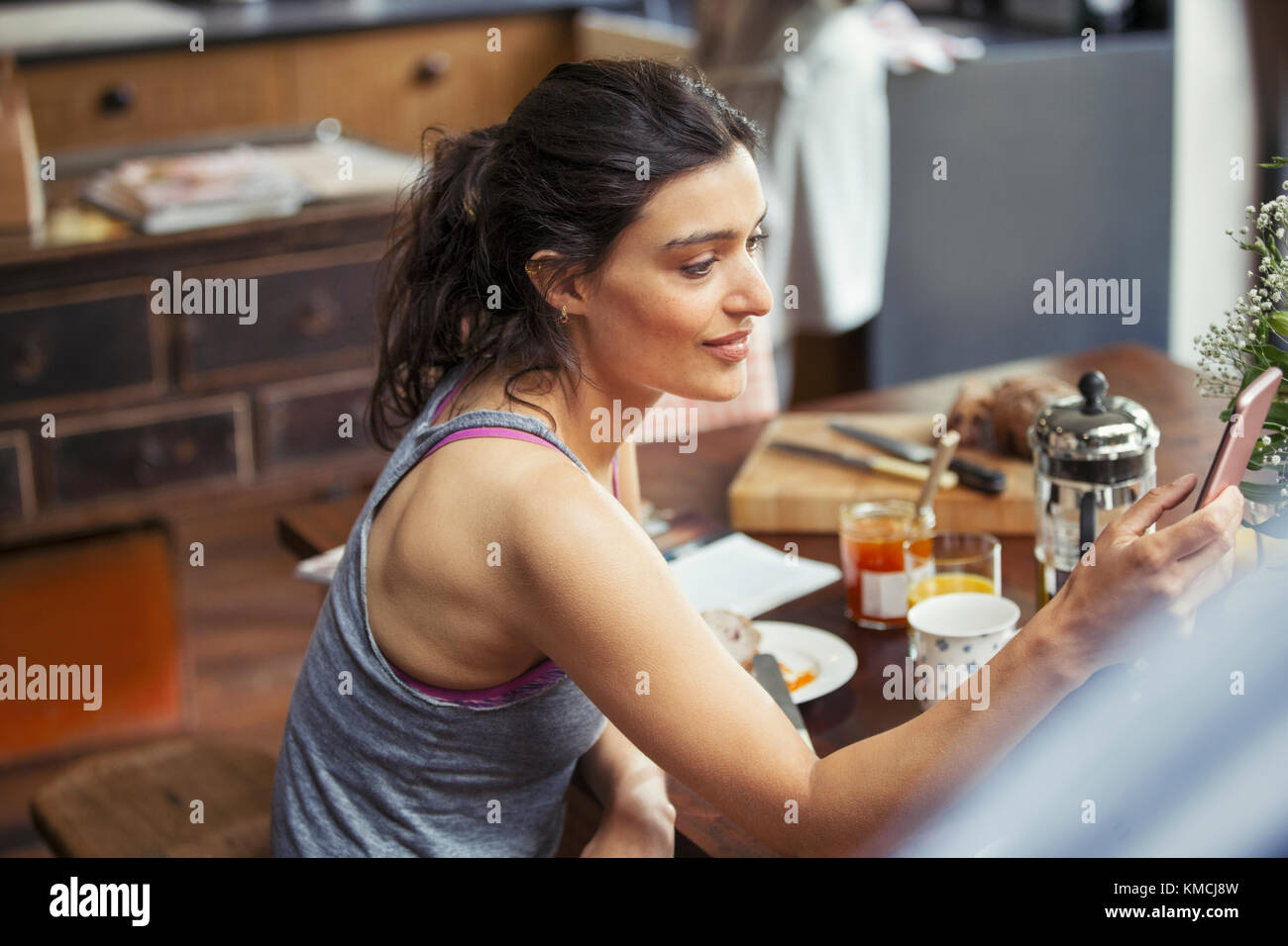 Mujer joven enviando mensajes de texto con un teléfono inteligente en la mesa de desayuno Foto de stock