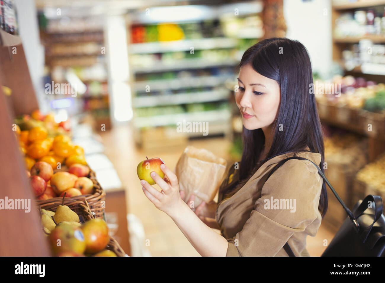 Mujer joven de compras, examinando la manzana en la tienda de comestibles Foto de stock