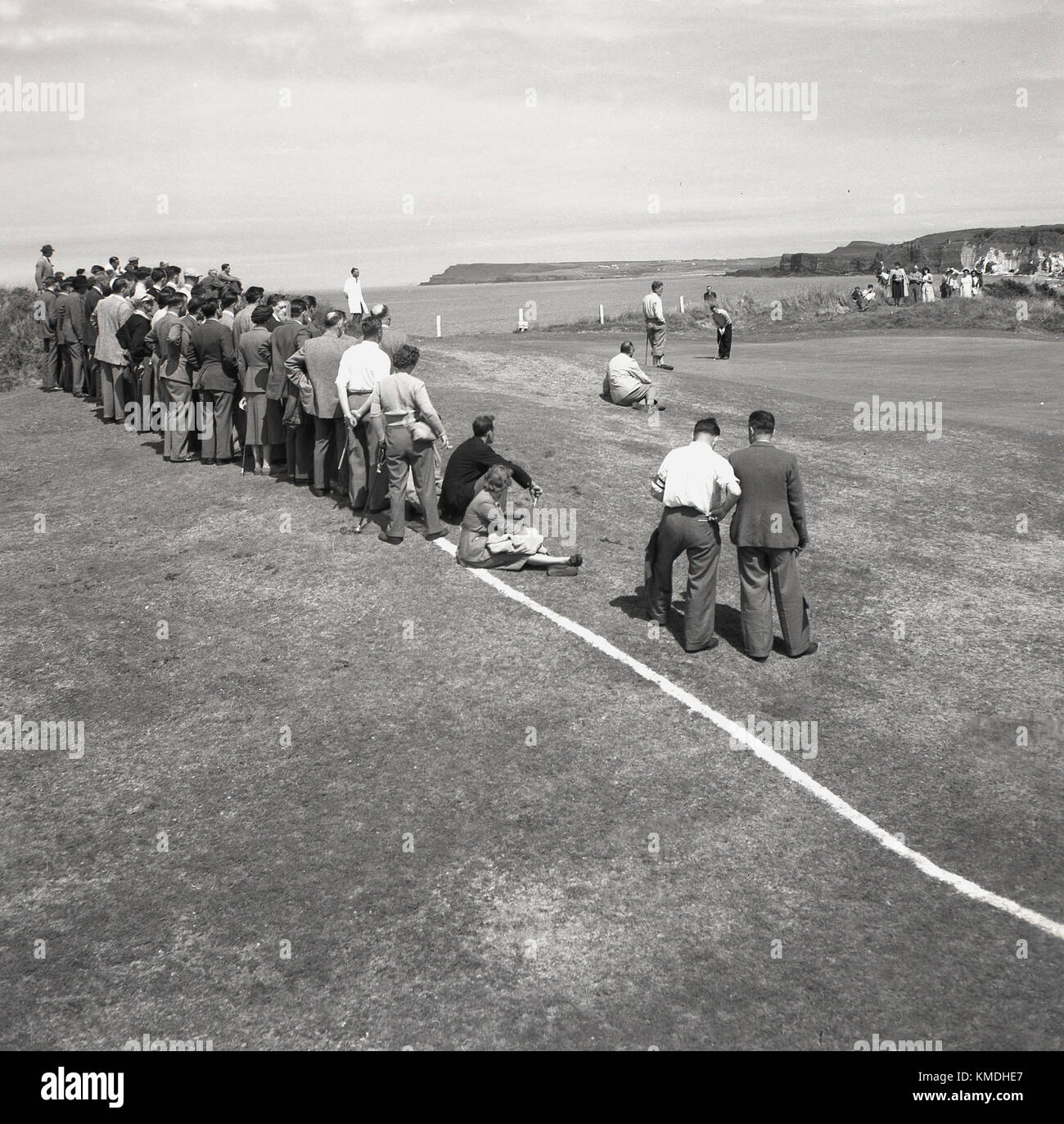 1951, histórico, en el Royal Portrush Golf Club en la costa de Antrim, Irlanda del Norte, se celebra el Campeonato Abierto Británico - ahora conocido simplemente como el Campeonato Abierto - con espectadores reunidos en torno a uno de los verdes costeros para ver a los golfistas jugar. Ahora conocido simplemente como 'The Open', este evento fue ganado por el golfista inglés Max Faulkner, su única victoria importante. Foto de stock
