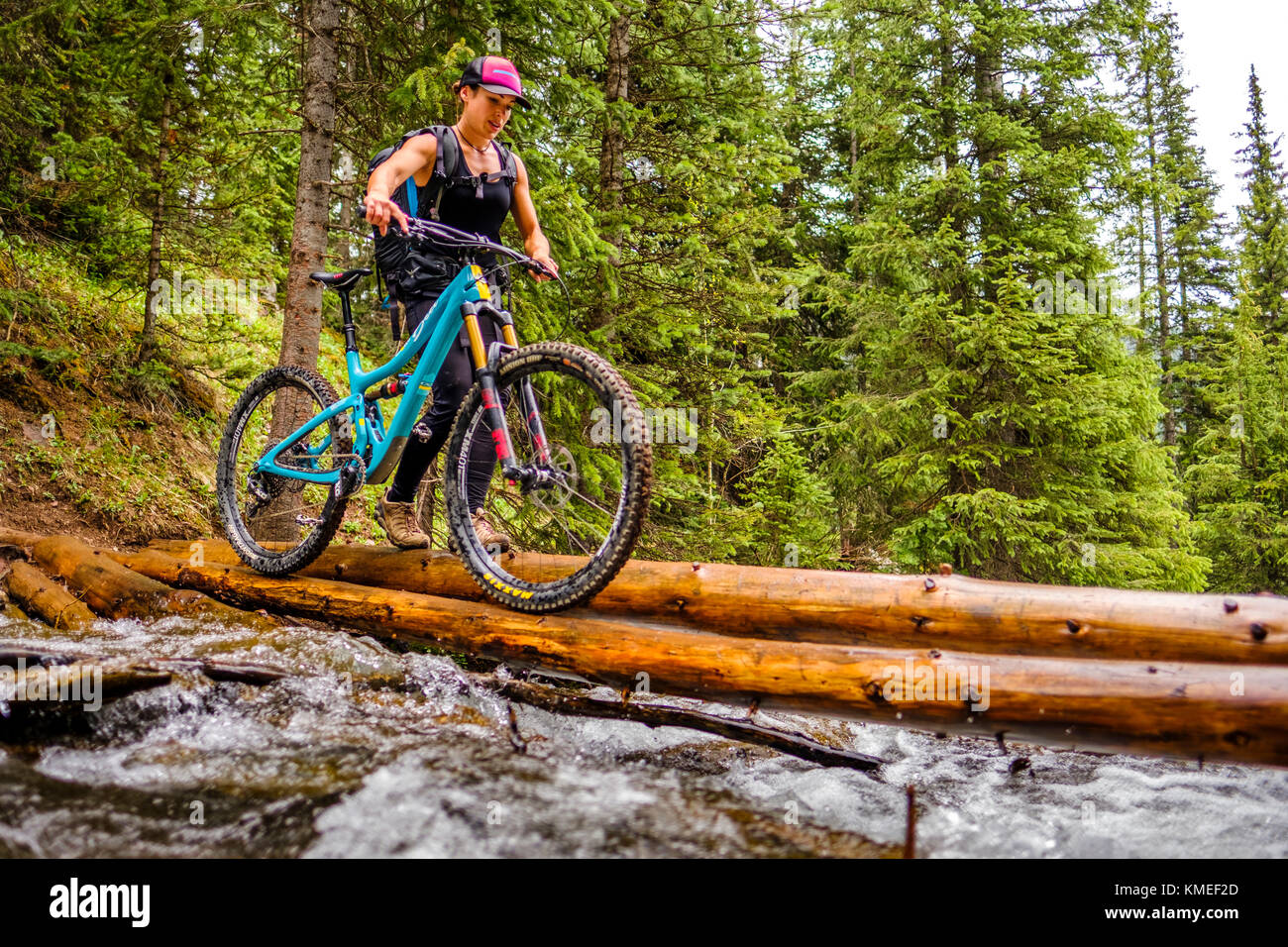 Mujer en el bosque cruza el puente registro con bicicleta de montaña sobre el hielo de lagos trail, EE.UU. Foto de stock