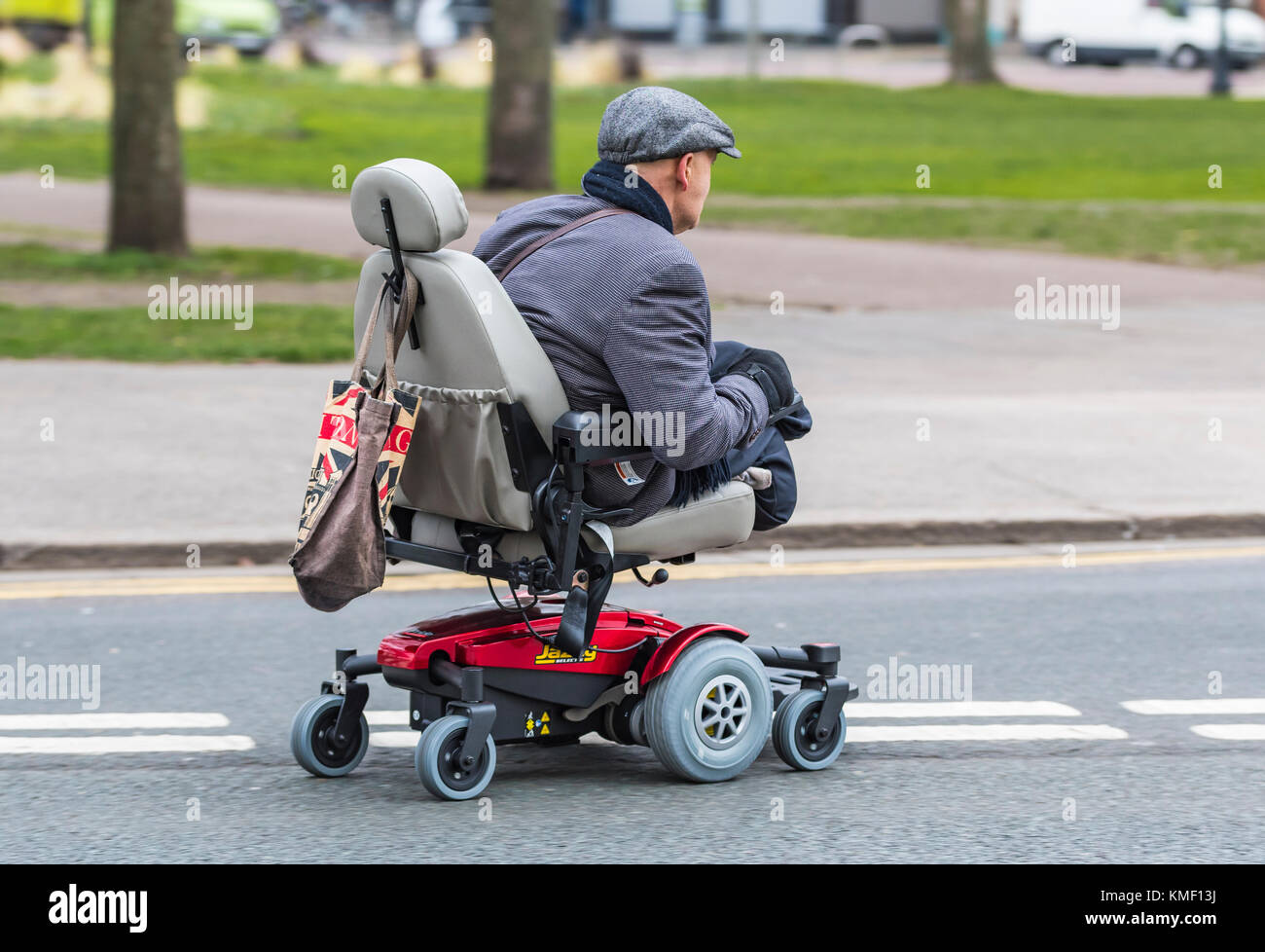 Doble amputado hombre sin piernas viajando en un scooter de movilidad en una carretera en el Reino Unido. Foto de stock