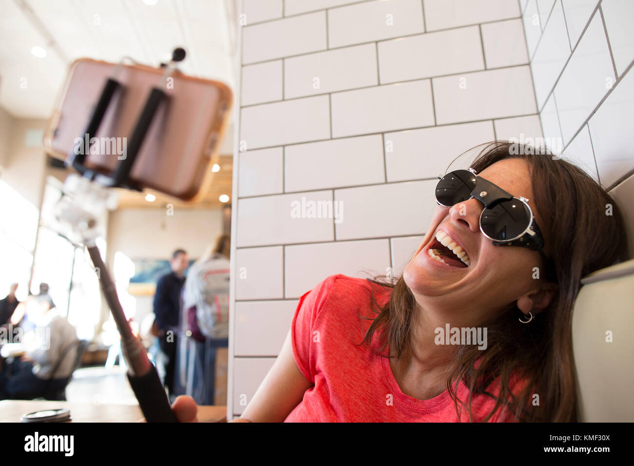 Mujer riendo mientras toma selfie en cafe con selfie stick,Santa Cruz, California, EE.UU. Foto de stock