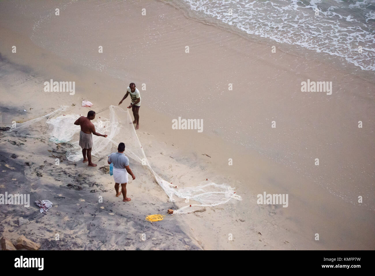 VARKALA, INDIA - alrededor de febrero de 2017: tres pescadores desplegado y limpiar una red de pesca después regresaron a la orilla, en Varkala Beach en la India. Foto de stock