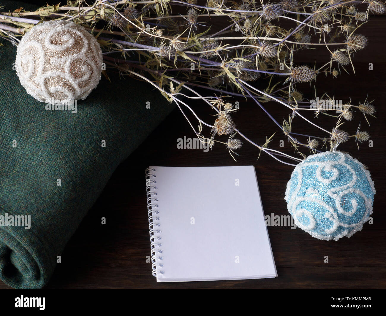 Un cálido suéter verde, flores secas, bolas de navidad y un bloc de notas acostarse sobre una mesa de roble. Foto de stock