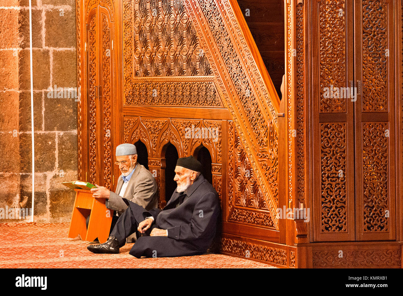 Ancianos musulmana turca hombres sentados en la mezquita y uno de ellos lee Corán dentro de la mezquita Ulu, en Erzurum, Turquía. Foto de stock
