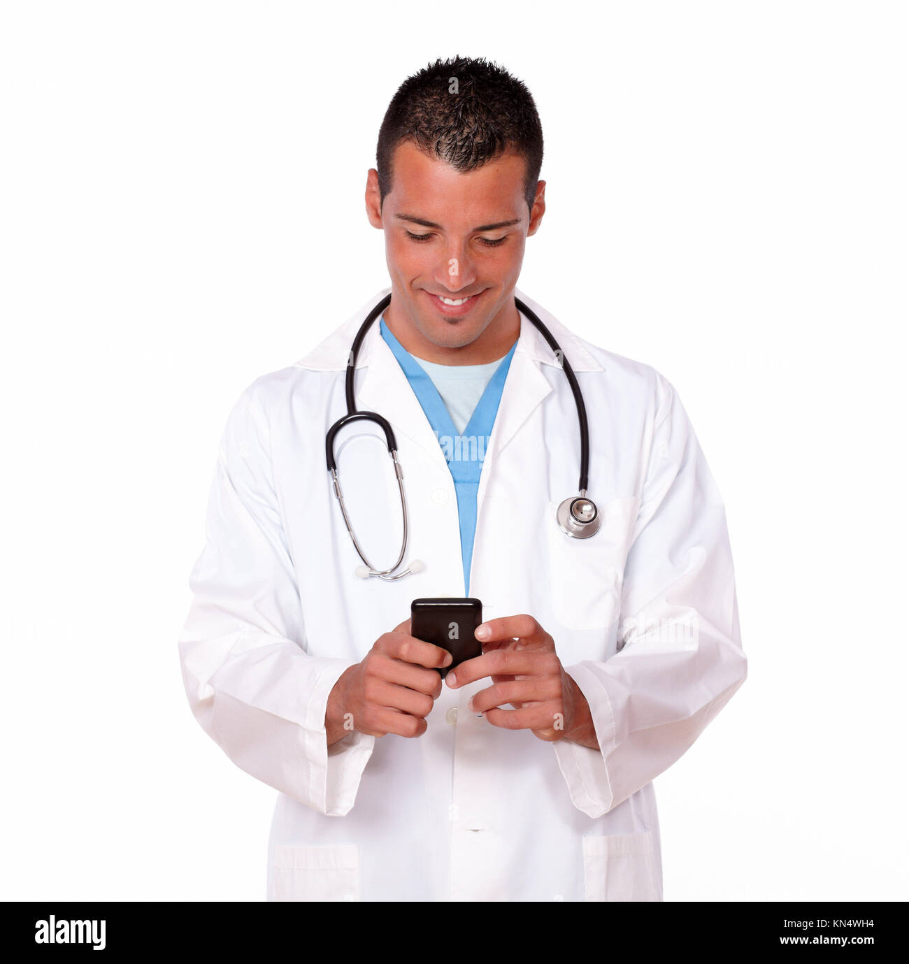 Retrato de un guapo 20-24 años médico varón texting un mensaje con su celular mientras está de pie sobre el aislamiento del fondo. Foto de stock