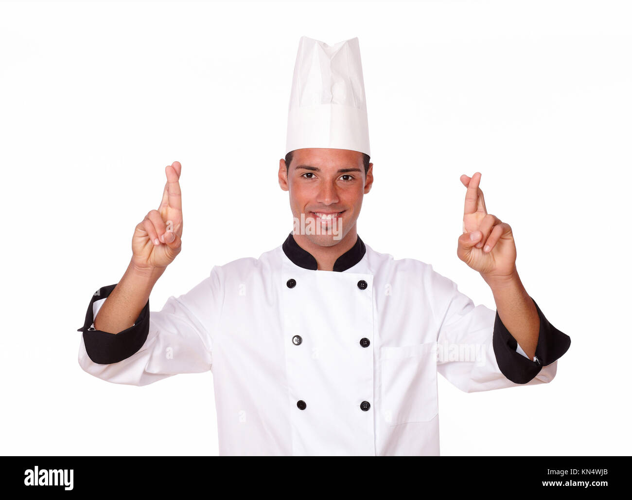 Retrato de 20-24 años guapo joven chef en blanco uniforme cruza los dedos mientras sonríe a usted sobre el aislamiento del estudio. Foto de stock