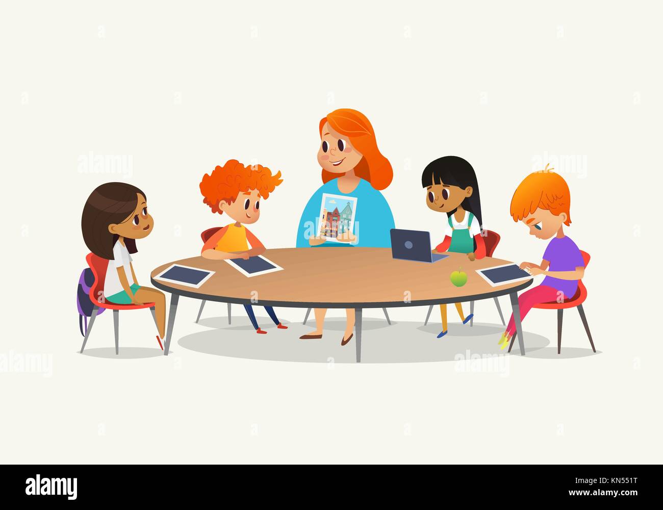 Pelirroja maestra mostrando imagen a niños sentados alrededor de la mesa  redonda a clase con ordenador portátil y Tablet PC. Los niños usar gadgets  durante la lección en la escuela primaria. Colorida