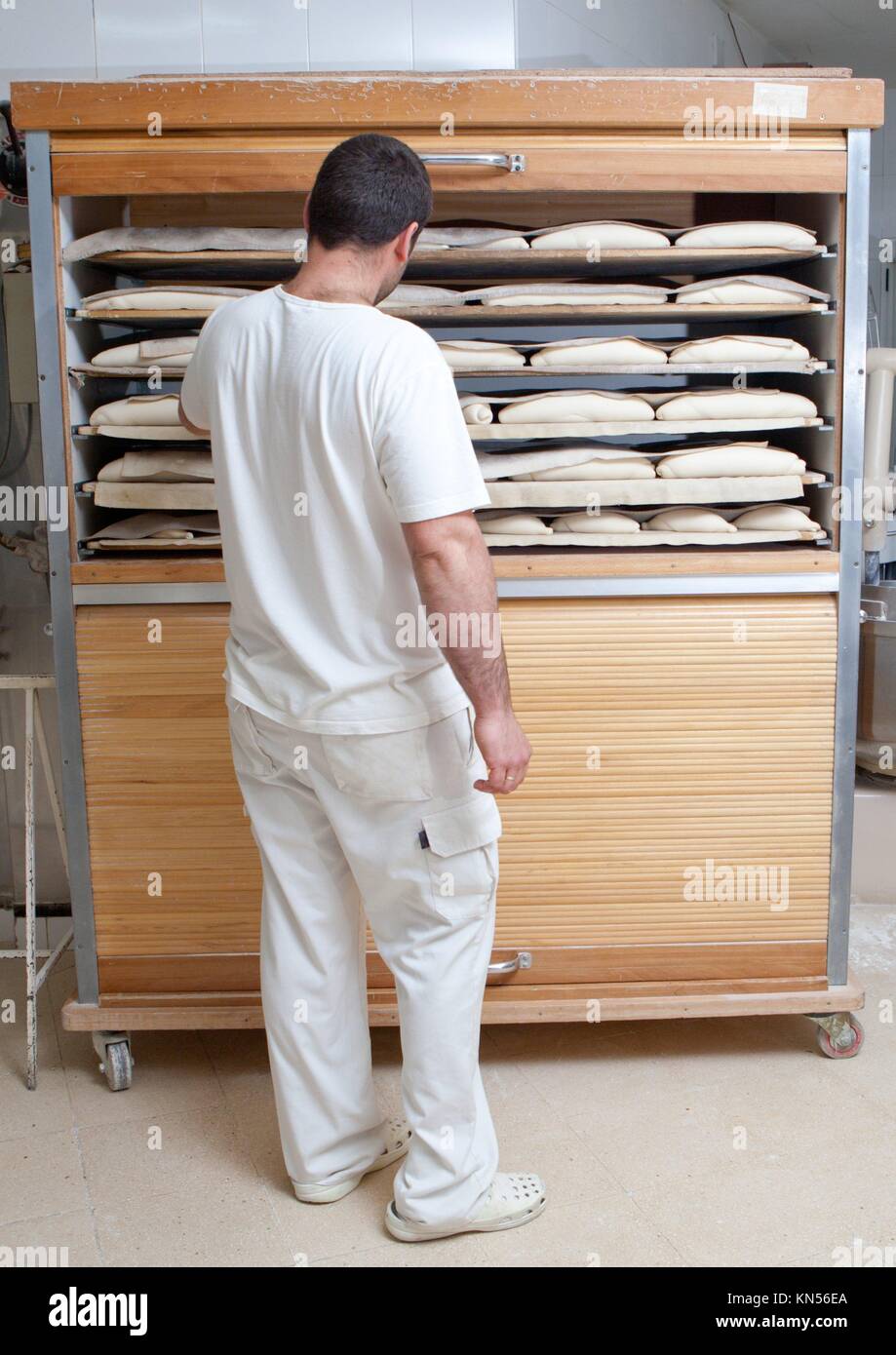 Comprobación de Baker trozos de pan en el armario de madera de fermentación. Proceso de fabricación de pan español. Foto de stock