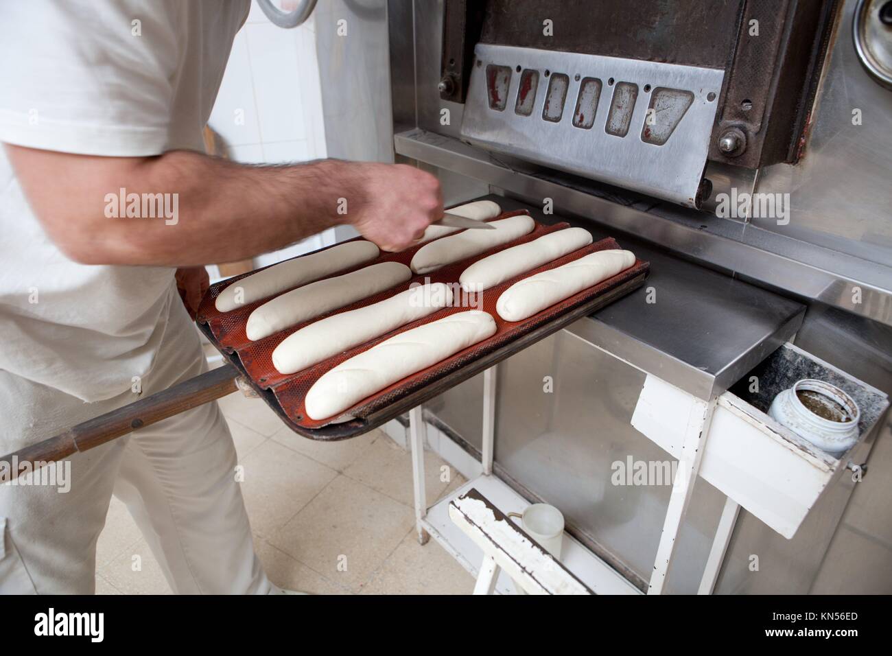 Baker haciendo patrones en materias pan con un cuchillo para dar forma a la masa antes de la cocción. Proceso de fabricación de pan español. Foto de stock
