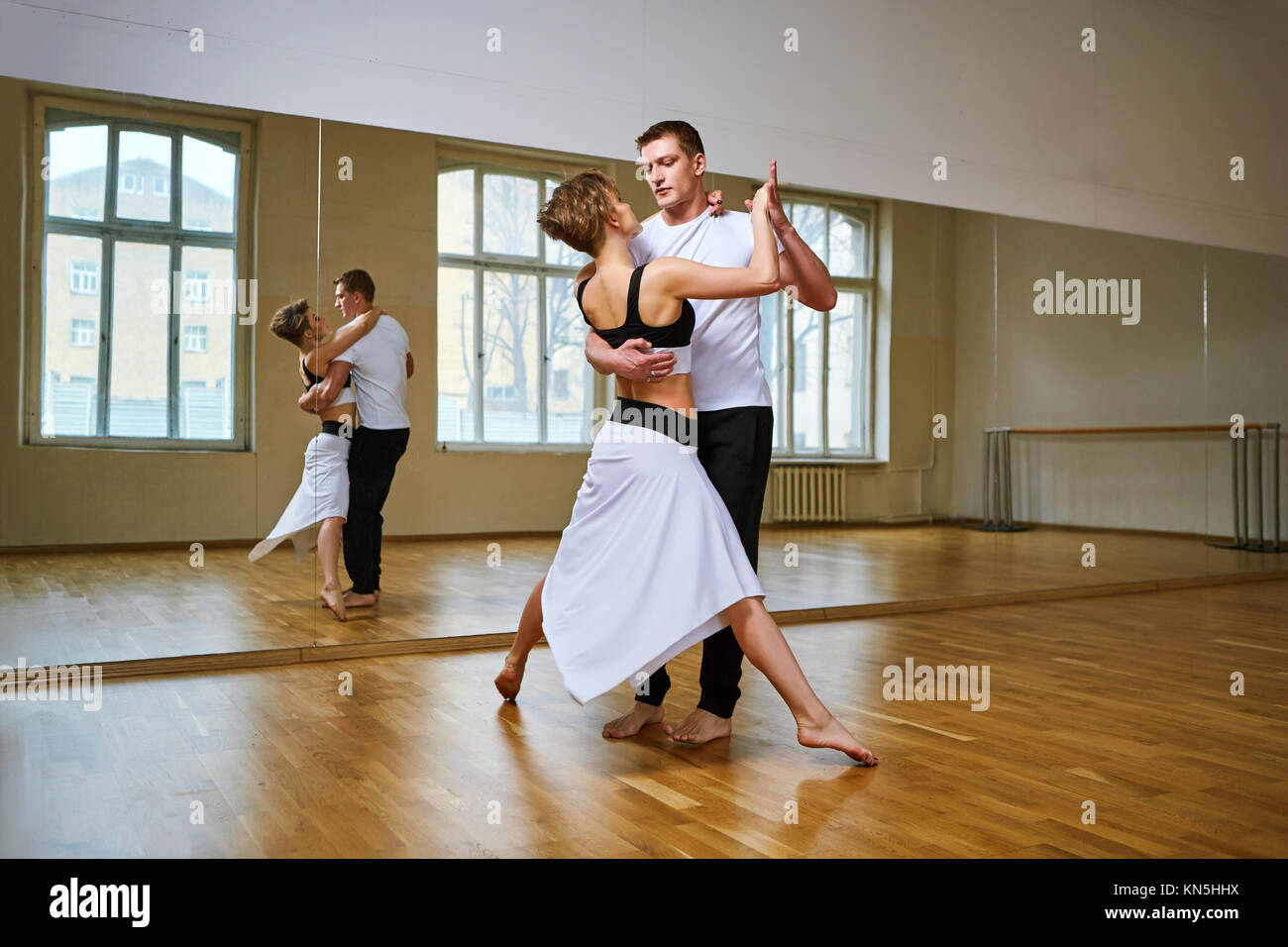 Hermosa pareja bailando tango. joven en blanco y negro y el hombre vestido  de ropa deportiva que practica en estudio de baile sala de espejo. Copie el  espacio Fotografía de stock -