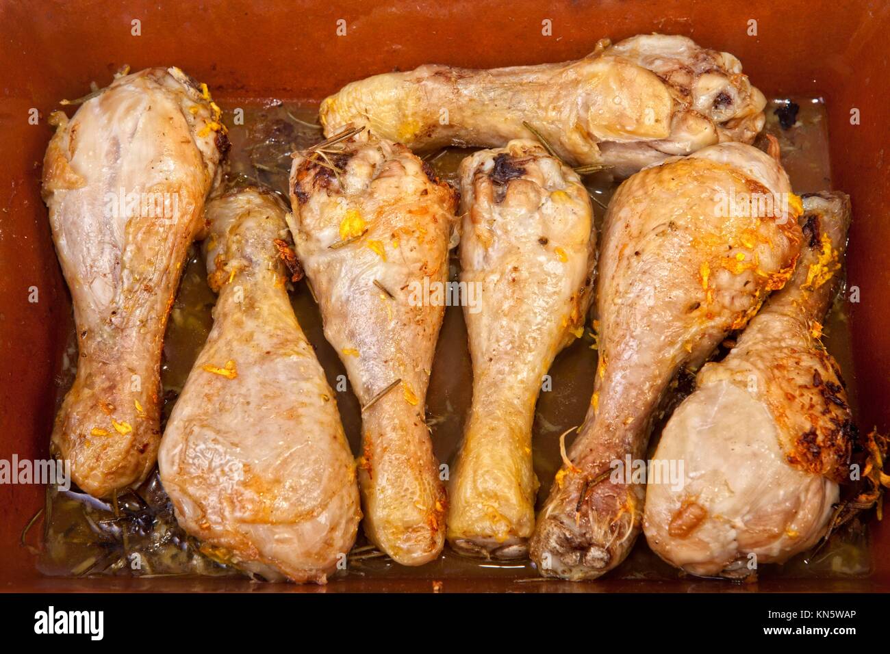 Piernas de pollo cocido al horno con hierbas en una cacerola de barro vidriado. Foto de stock