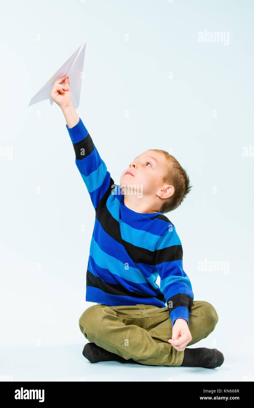 Muchacho feliz jugando con avión de papel en studio, fondo de color azul claro. Foto de stock