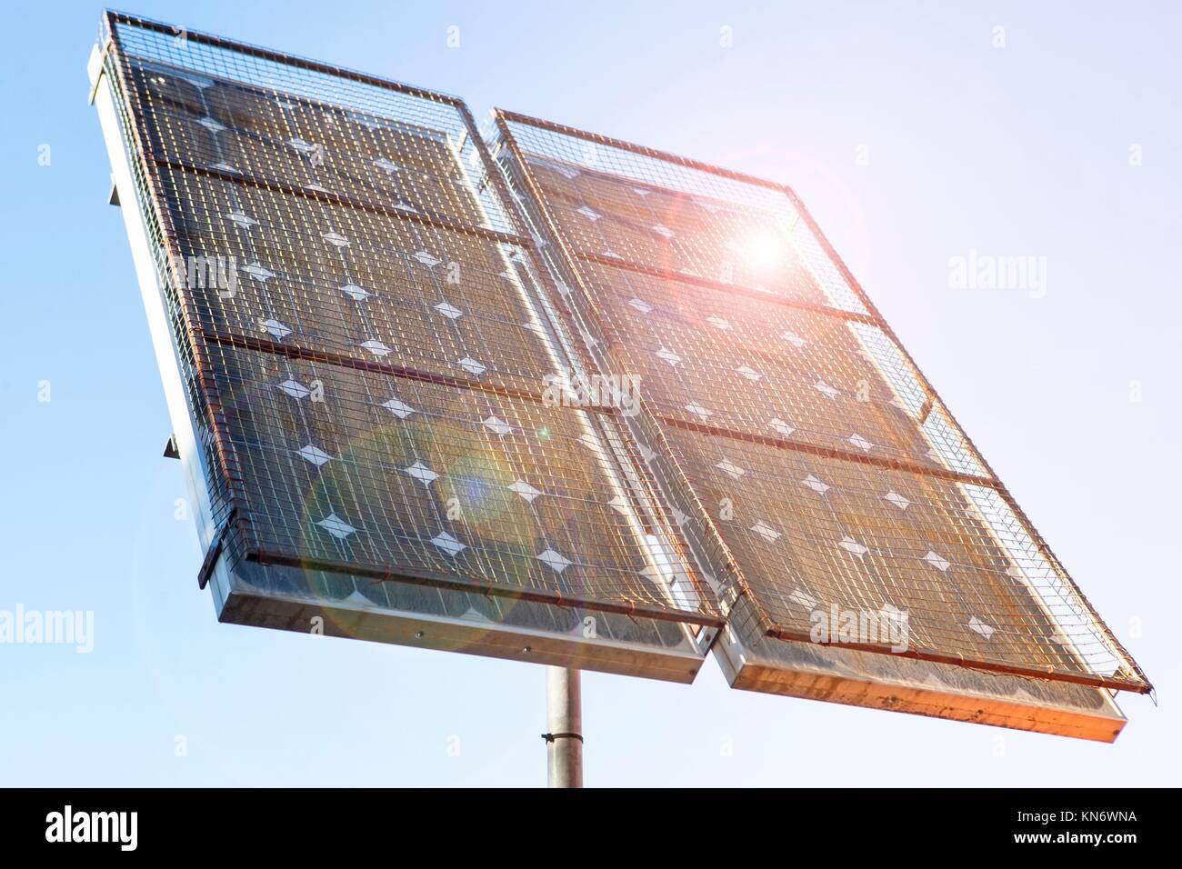 Panel solar instalado en la parte superior de un poste con el enrejado metálico protegido e iluminado con el sol brilla. Foto de stock