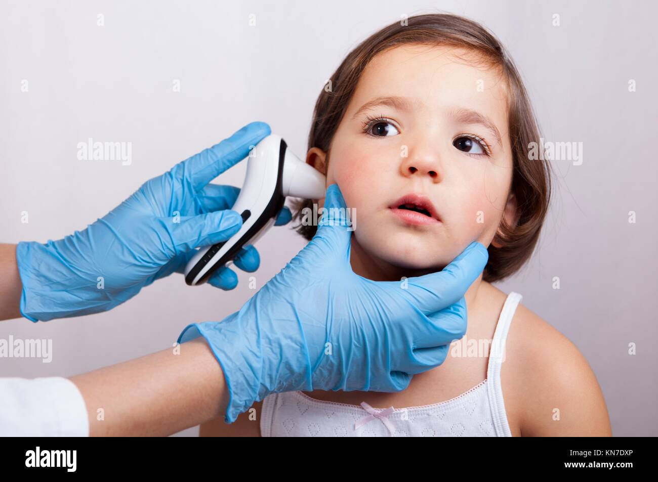 Doctor en medición de temperatura relajado niña con oído hablar termómetro electrónico. Aislado sobre fondo blanco. Foto de stock