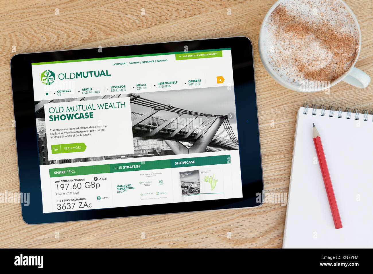El sitio web de Old Mutual en un dispositivo tablet iPad que descansa sobre una mesa de madera junto a un bloc de notas y lápiz y una taza de café (Editorial) Foto de stock