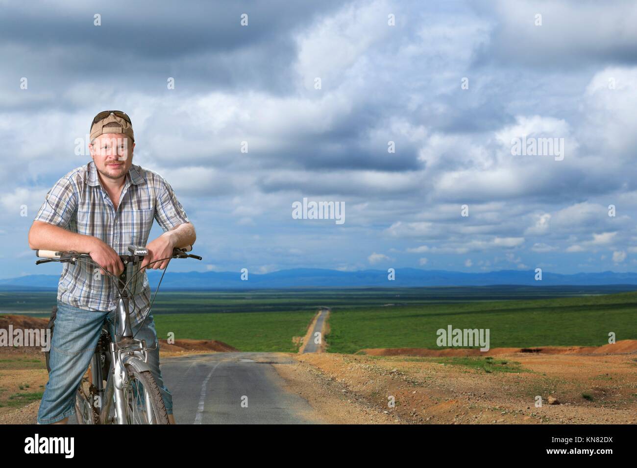 Hombre de pie turística con una bicicleta en la carretera entre los campos. Foto de stock