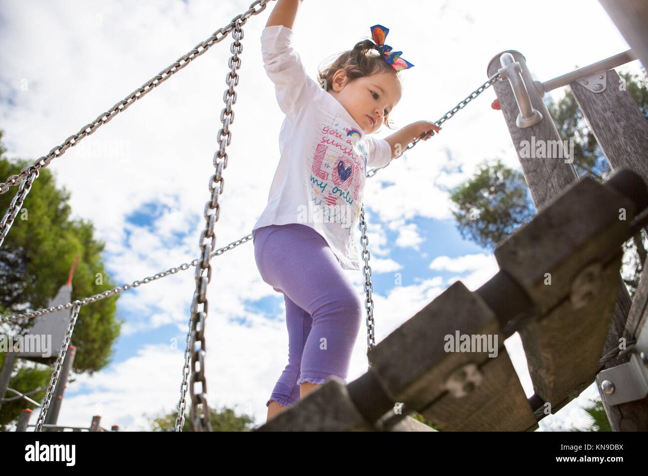 Hermosa niña subir un pequeño puente colgante de madera en el patio de recreo. Foto de stock