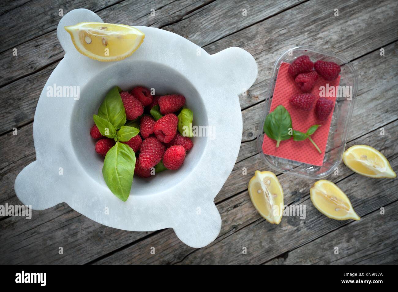 Mortero con frambuesas frescas, las hojas de albahaca y rodajas de limón, encima de disparo. Foto de stock