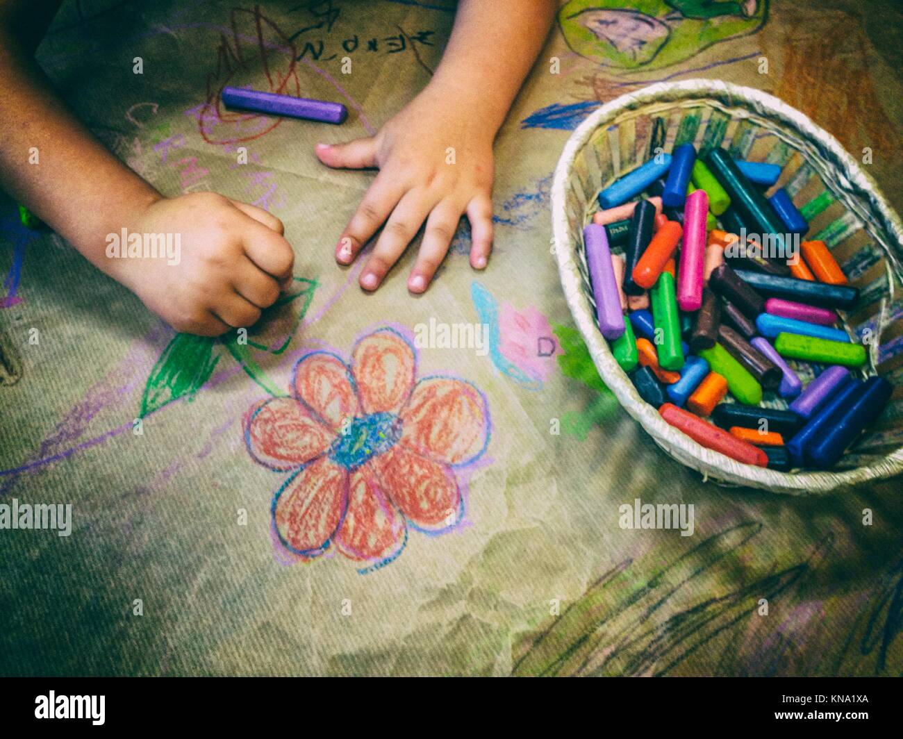 Dibujo infantil con una canasta de lápices de cera sobre la artesanía del papel de embalaje. Un alto ángulo de visualización. Foto de stock
